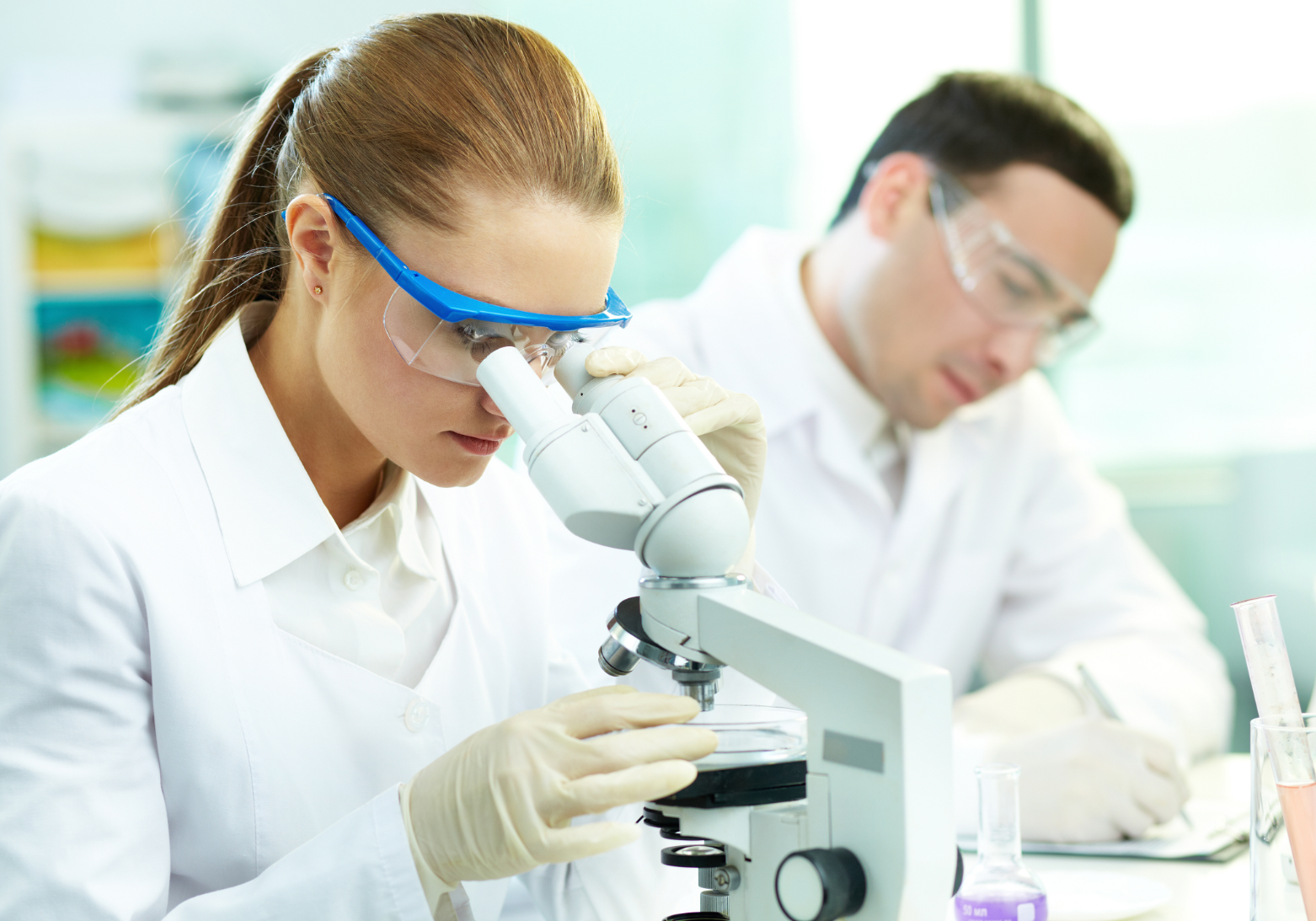 cercetatori care se uta la microscop